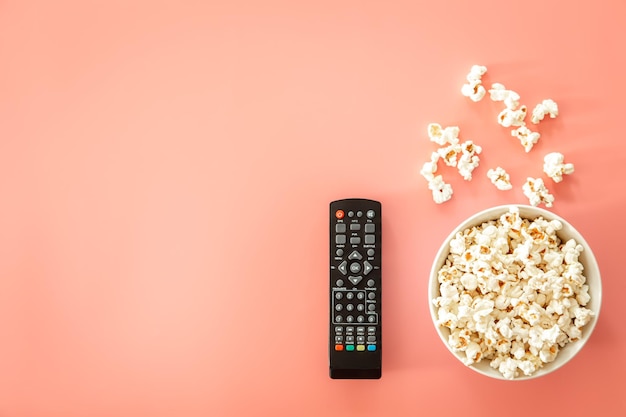 Telecomando e piatto con popcorn su fondo rosa piatto