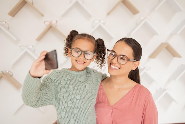 Telefona madre e figlio si fanno un selfie dall'optometrista con gli occhiali nuovi dopo aver acquistato uno sconto per la famiglia Sorridi mamma e ragazza felice che acquistano nuove montature per una vista o una vista migliori in un negozio al dettaglio