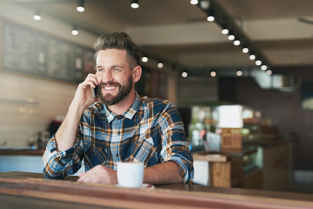 telefonata caffetteria e uomo con sorriso e bere bevanda caffeina e cappuccino ristorante mensa e persona felice rilassarsi con smartphone per la discussione comunicazione e conversazione