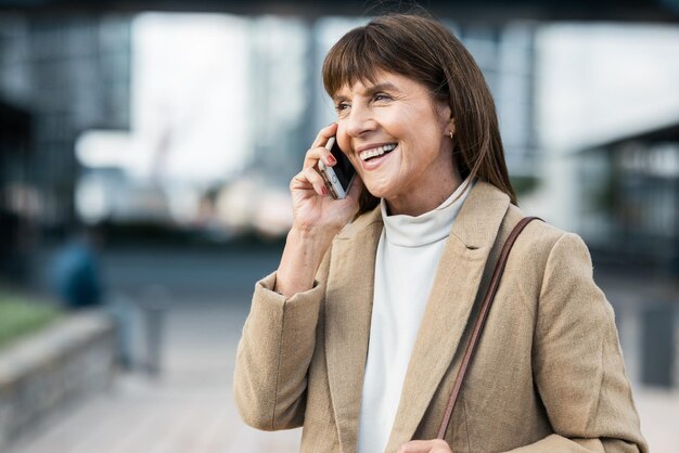 Telefonata di comunicazione e donna matura in città che parla parlando conversando online Connessione tecnologica e donna anziana che cammina nella città urbana utilizzando smartphone sorridente e felice