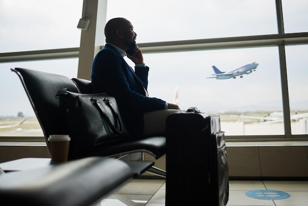 Telefonata uomo nero e bagaglio all'aeroporto per viaggio d'affari o comunicazione in attesa del volo Maschio afroamericano in conversazione o discussione su smartphone pronto a salire a bordo dell'aereo