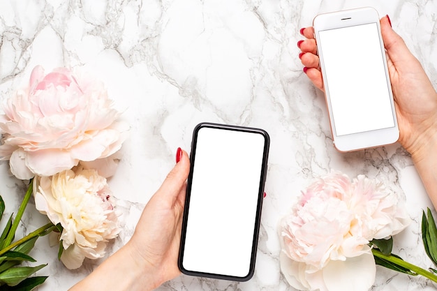 Telefoni cellulari in mani femminili con fiori di piony su uno sfondo di marmo, utilizzando il concetto di tecnologia per le vacanze - San Valentino, festa della donna e festa della mamma. Floristica e decorazione