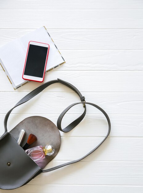 Telefono, borsa elegante e profumi su sfondo bianco. Bella disposizione piatta. Cose per donna d'affari. Agenda del taccuino. Kit del make up.