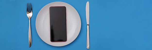 Telefono cellulare che giace in un piatto bianco vicino a forchetta e coltello