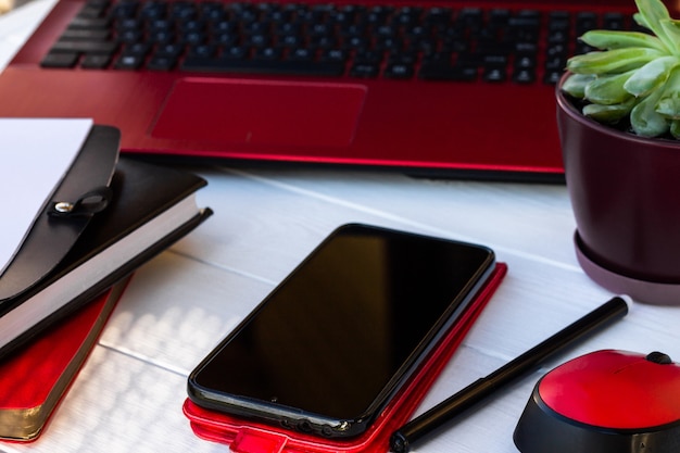 Telefono cellulare, diario e computer portatile rossi su un fondo di legno bianco.