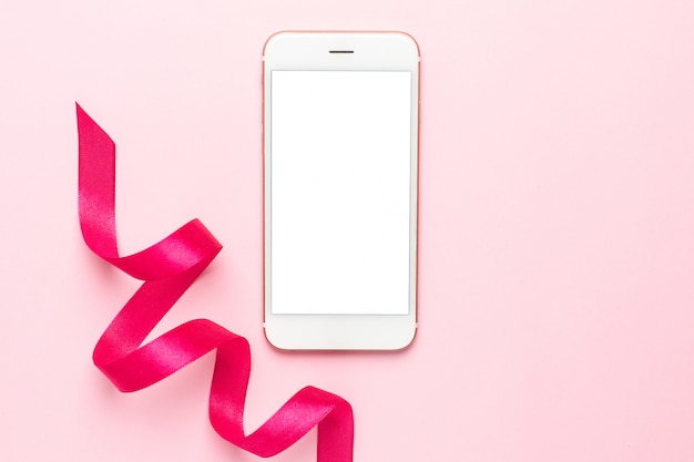 Telefono cellulare e nastro regalo sul rosa