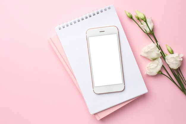 Telefono cellulare, fiore bianco e taccuino sul rosa