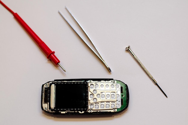 Telefono cellulare smontato sul tavolo di un ingegnere meccanico durante la riparazione Pinzette e cacciavite per la riparazione di gadget elettronici su sfondo bianco