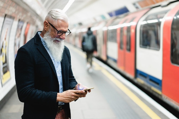 Telefono cellulare uomo anziano hipster mentre attende il treno della metropolitana Concentrarsi sulla mano sinistra