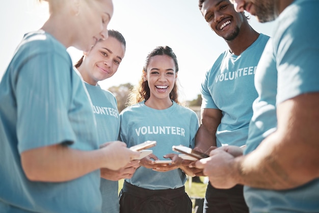 Telefono del team di volontari e ritratto di persone nel parco per chat online sui social media o aggiornamento del sito web di beneficenza Lavoro di squadra del servizio comunitario e gruppo felice su smartphone per pulire o riciclare all'aperto