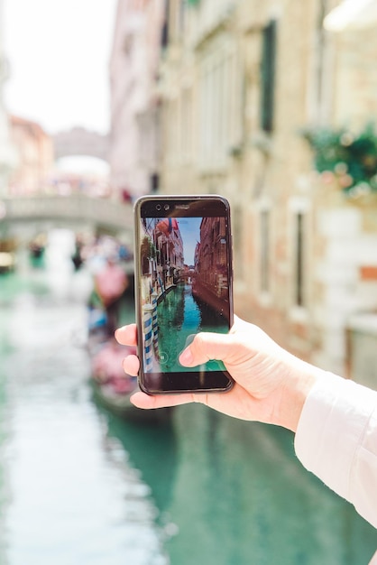 Telefono della tenuta della mano della donna che cattura la foto dei canali di venezia con le vacanze estive delle gondole