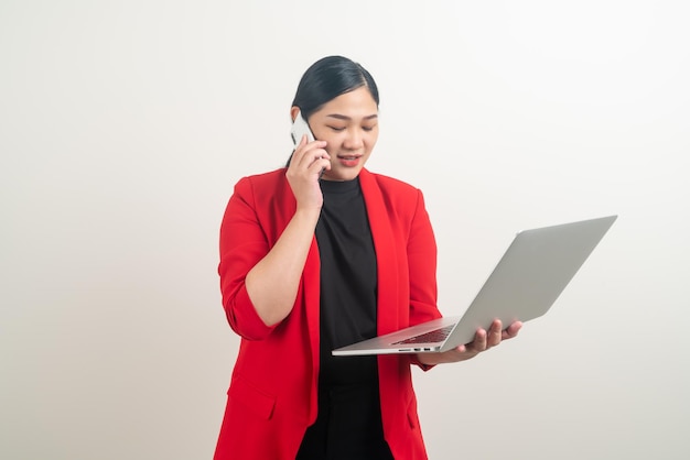 Telefono di conversazione della donna asiatica di affari con il computer portatile della tenuta della mano