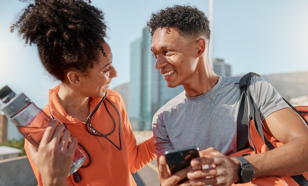 Telefono di coppia e allenamento in città per l'esercizio sorriso e benessere per rilassarsi e allenarsi Salute persone di colore e smartphone per il fitness all'aperto e in salute insieme parlando felice e bottiglia d'acqua