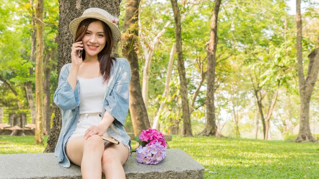 Telefono di uso della ragazza di modo nel parco del giardino.