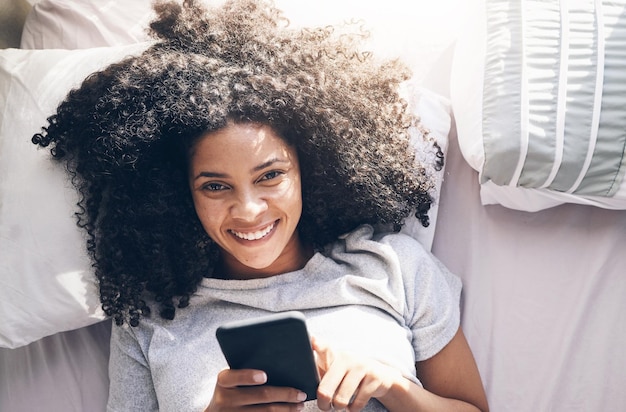 Telefono donna nera e vista dall'alto nella camera da letto di casa per messaggi sui social media o navigazione in Internet al mattino Letto verticale relax e donna con smartphone mobile per scorrimento web o networking