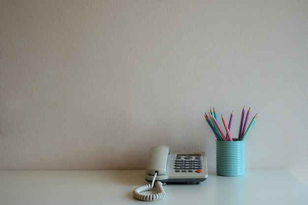 Telefono e matite pastello nel vetro blu sulla scrivania sullo sfondo del muro grigio