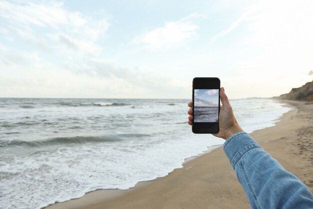 Telefono femminile della stretta della mano con la fabbricazione del selfie sul mare