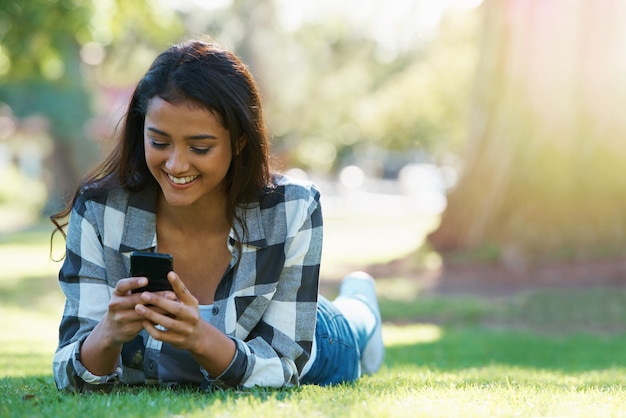 Telefono grass o donna felice nel parco per i social media per chiacchierare su internet post o notifica sul sito web sorriso della natura o persona femminile su app mobile per messaggi di rete o digitare online per rilassarsi