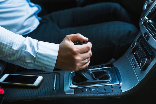 Telefono mobile vicino alla mano dell&#39;uomo che sposta la leva del cambio mentre si guida l&#39;auto