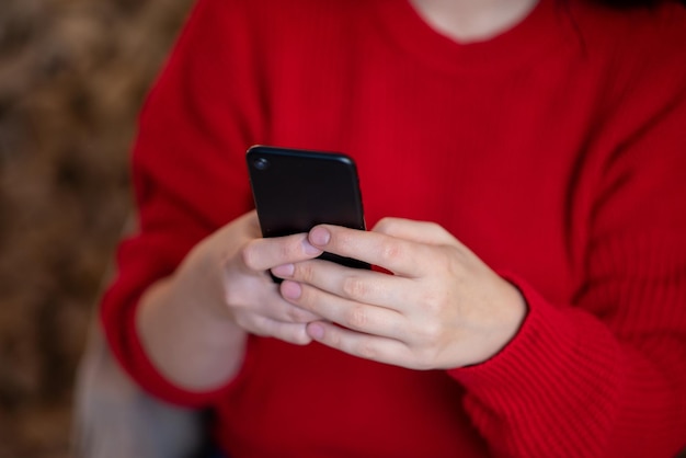 Telefono nero nelle mani delle donne in un maglione rosso