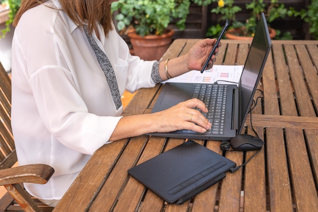 Telelavoro della donna bianca in giardino con telefono cellulare e laptop.