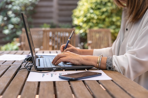 Telelavoro donna bianca in giardino con laptop e notebook.