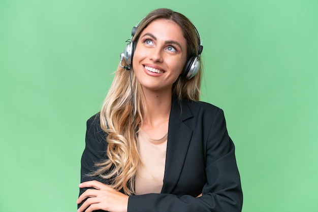 Telemarketer bella donna uruguaiana che lavora con un auricolare su sfondo isolato guardando in alto mentre sorride