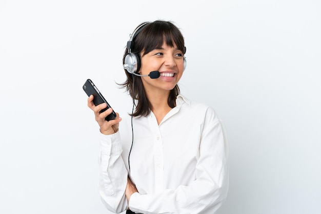 Telemarketer donna di razza mista che lavora con un auricolare isolato su sfondo bianco mantenendo una conversazione con il telefono cellulare