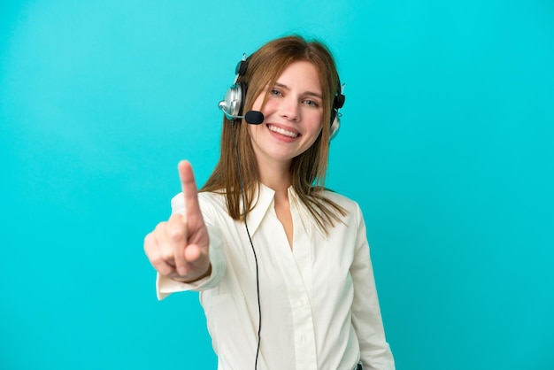 Telemarketer Donna inglese che lavora con un auricolare isolato su sfondo blu che mostra e solleva un dito