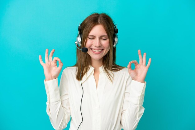 Telemarketer Donna inglese che lavora con un auricolare isolato su sfondo blu in posa zen