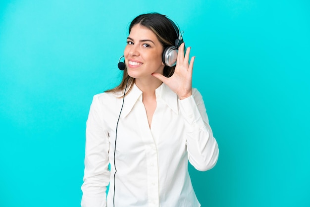 Telemarketer Donna italiana che lavora con un auricolare isolato su sfondo blu ascoltando qualcosa mettendo la mano sull'orecchio