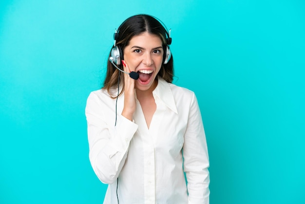 Telemarketer Donna italiana che lavora con un auricolare isolato su sfondo blu con espressione facciale sorpresa e scioccata