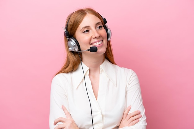 Telemarketer donna rossa che lavora con un auricolare isolato su sfondo rosa felice e sorridente