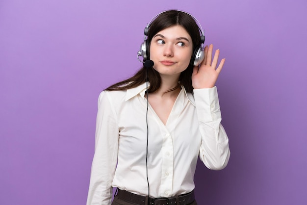 Telemarketer Donna russa che lavora con un auricolare isolato su sfondo viola ascoltando qualcosa mettendo la mano sull'orecchio