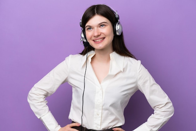 Telemarketer Donna russa che lavora con un auricolare isolato su sfondo viola in posa con le braccia all'anca e sorridente