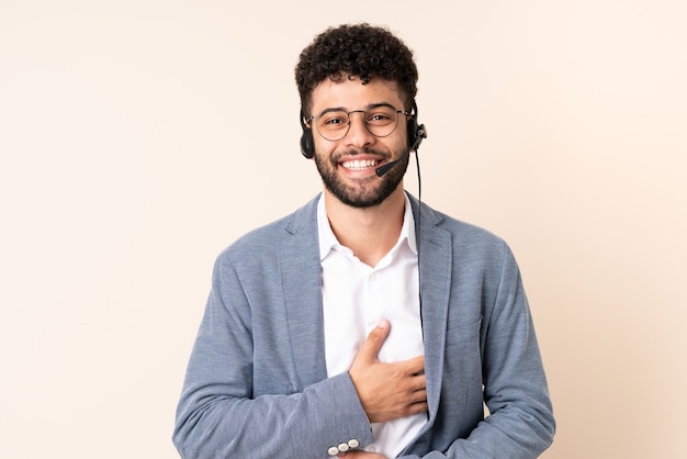 Telemarketer marocchino uomo che lavora con un auricolare isolato sul muro beige sorridente molto