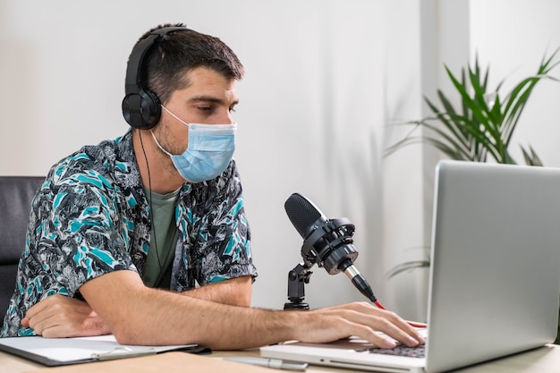 Telemarketer o podcast uomo che lavora con il laptop e parla su un auricolare con maschera facciale in ufficio