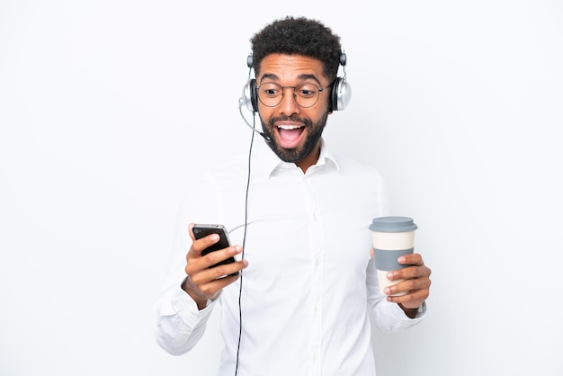 Telemarketer Uomo brasiliano che lavora con un auricolare isolato su sfondo bianco tenendo il caffè da portare via e un cellulare