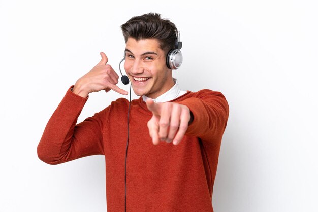 Telemarketer uomo caucasico che lavora con un auricolare isolato su sfondo bianco facendo il gesto del telefono e indicando la parte anteriore