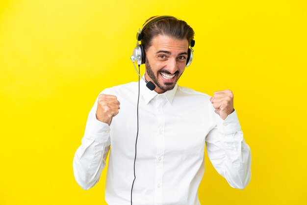 Telemarketer uomo caucasico che lavora con un auricolare isolato su sfondo giallo che celebra una vittoria in posizione di vincitore