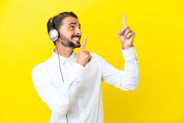 Telemarketer uomo caucasico che lavora con un auricolare isolato su sfondo giallo che punta con il dito indice una grande idea