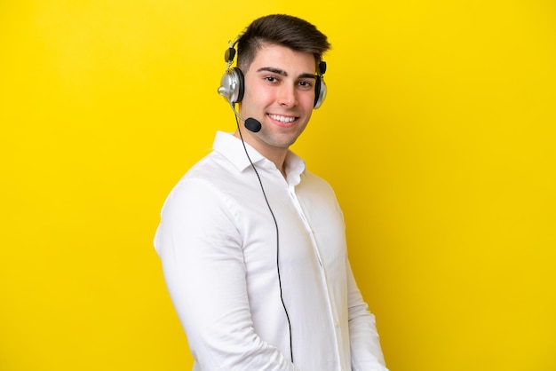 Telemarketer uomo caucasico che lavora con un auricolare isolato su sfondo giallo con le braccia incrociate e guardando avanti