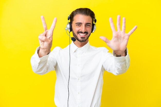 Telemarketer uomo caucasico che lavora con un auricolare isolato su sfondo giallo contando sette con le dita