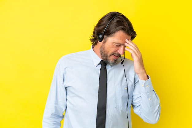 Telemarketer uomo olandese che lavora con un auricolare isolato su sfondo giallo ridendo