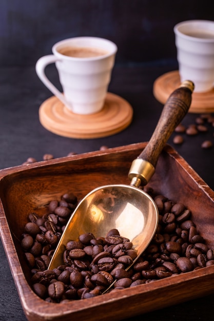 Tema del caffè. Tazze di caffè e piatto caldi con i chicchi di caffè sulla tavola di legno nera.