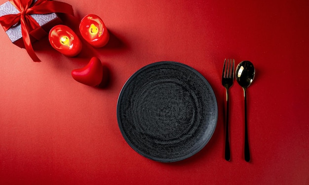 Tema rosso di San Valentino con piatti vuoti neri, cuore e candele e confezione regalo sullo sfondo.