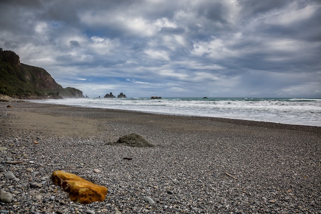 Tempesta che si avvicina a una roccia arancione su una spiaggia in Nuova Zelanda