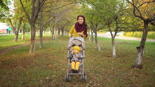 Tempo d'autunno. La mamma fa rotolare la carrozza con la figlia piccola lungo il vicolo del parco ammirando il bellissimo paesaggio autunnale in una calda giornata di sole