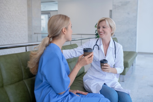 Tempo del caffè. Due operai medici femminili sorridente che si siedono sul sofà, bevendo caffè