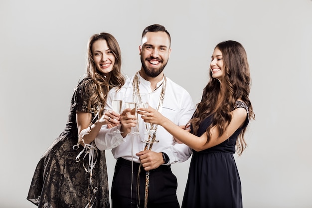 Tempo di festa. Due belle ragazze vestite con abiti eleganti e un bell'uomo con la camicia bianca tengono bicchieri di champagne.